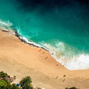 Stunning aerial view of Bali's beach with turquoise waves crashing on golden sand.